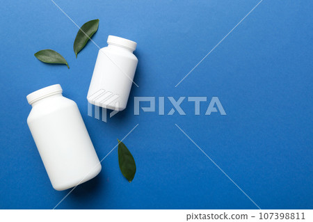 supplement pills with medicine bottle health care and medical top view. Vitamin tablets. Top view mockup bottle for pills and vitamins with green leaves, natural organic bio supplement, copy space 107398811