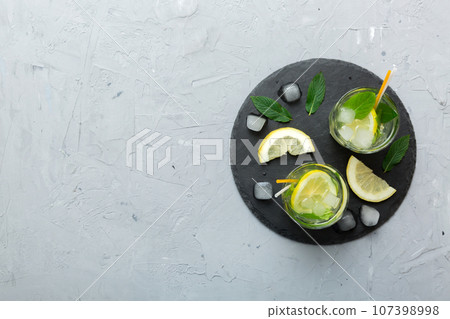 Caipirinha, Mojito cocktail, vodka or soda drink with lime, mint and straw on table background. Refreshing beverage with mint and lime in glass top view flat lay Caipirinha, Mojito cocktail, vodka or soda drink with lime, mint and straw on table background. Refreshing beverage with mint and lime in glass top view flat lay 107398998