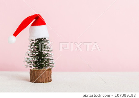 One small Christmas tree with santa hat on colored background. new year decoration with copy space One small Christmas tree with santa hat on colored background. new year decoration with copy space 107399198