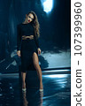 Sexy fashionable lady in black dress posing in studio on dark foil background 107399960