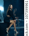 Sexy fashionable lady in black dress posing in studio on dark foil background 107399961