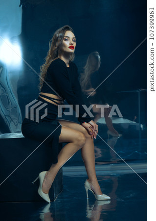 Sexy fashionable lady in black dress posing in studio on dark foil background 107399961