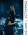 Sexy fashionable lady in black dress posing in studio on dark foil background 107399962