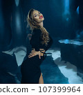 Sexy fashionable lady in black dress posing in studio on dark foil background 107399964