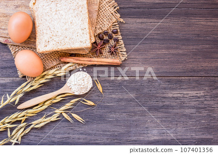 Ears of wheat and egg with slice of bread on a wooden table background. 107401356