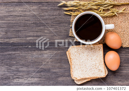 Ears of wheat and cup of coffee on a dark wooden table Ears of wheat and cup of coffee on a dark wooden table 107401372