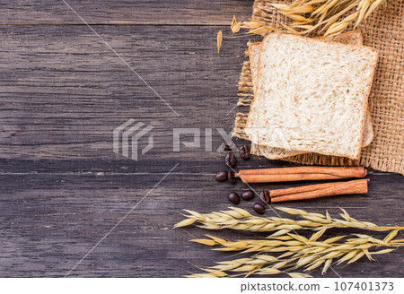 Ears of wheat and slice of bread on a dark wooden table Ears of wheat and slice of bread on a dark wooden table 107401373