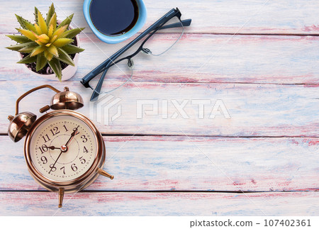 Retro alarm clock,glasses,cup of coffee and flower on a wooden table. Retro alarm clock,glasses,cup of coffee and flower on a wooden table. 107402361