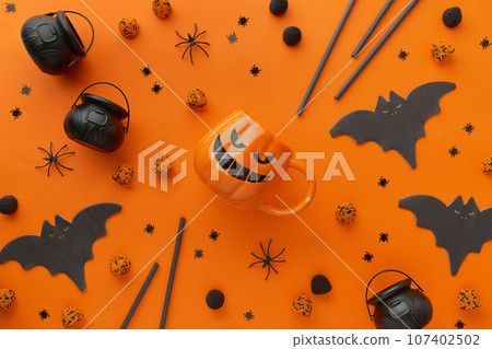 Pumpkin cup, gummy, straws, bat napkin on orange background. Halloween celebration concept Pumpkin cup, gummy, straws, bat napkin on orange background. Halloween celebration concept 107402502