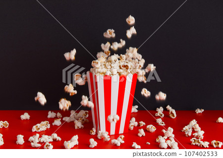 Striped box with popcorn on a red and black background Striped box with popcorn on a red and black background 107402533