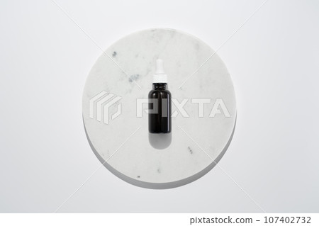 Face oil serum in dark glass bottle with dropper on marble circle white background. Clean minimalist high key skincare product shot top view 107402732