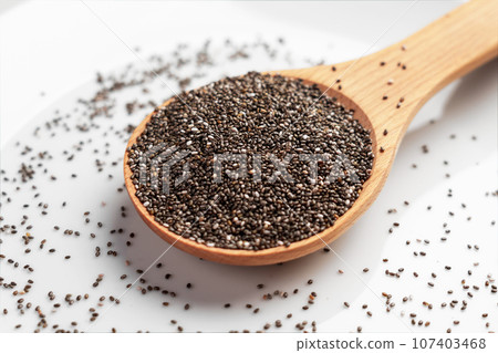 Wooden spoonful of wholesome chia seeds. Source of Omega 3 fatty acids on white ceramic surface close up Wooden spoonful of wholesome chia seeds. Source of Omega 3 fatty acids on white ceramic surface close up 107403468