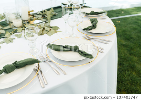 Open -air wedding banquet. The table is decorated with white plates and premium glasses for wine 107403747