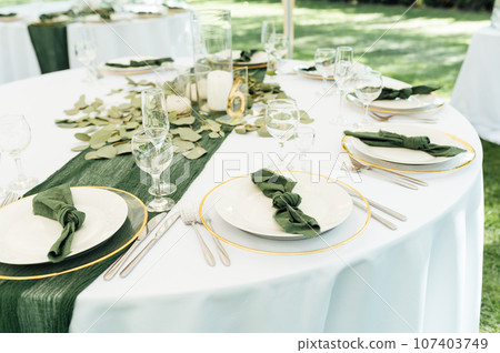 Open -air wedding banquet. The table is decorated with white plates and premium glasses for wine 107403749