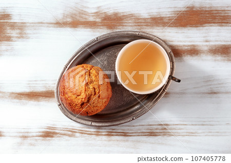 Orange muffin with tea on a rustic wooden kitchen table, on a vintage tray Orange muffin with tea on a rustic wooden kitchen table, on a vintage tray 107405778