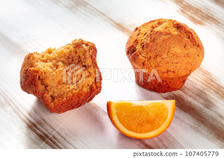 Broken orange muffins on a rustic wooden kitchen table, with the fresh fruit Broken orange muffins on a rustic wooden kitchen table, with the fresh fruit 107405779