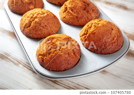 Orange muffins in a muffin tin on a rustic wooden kitchen table Orange muffins in a muffin tin on a rustic wooden kitchen table 107405780