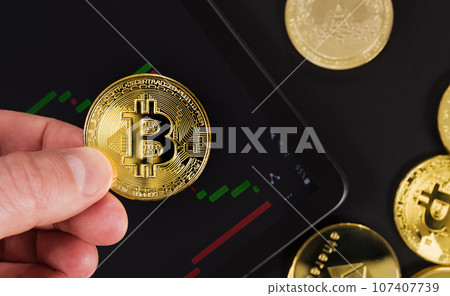 Hand holding Bitcoin over digital tablet by coins 107407739