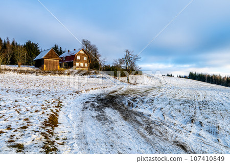 Hilly landscape with wooden rural house and first snow in early winter. Giant Mountains, Czech: Krkonose, Czechia Hilly landscape with wooden rural house and first snow in early winter. Giant Mountains, Czech: Krkonose, Czechia 107410849