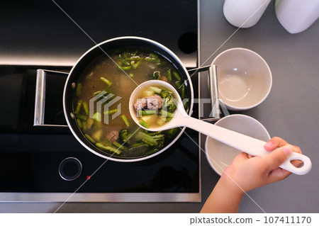 The girl serves the soup with a ladle. 107411170