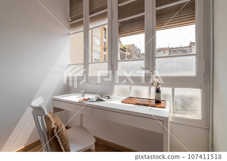 Cozy work table with chair and book tray and a vase of flowers next to the blinds on window. The concept of a working area in a hotel for traveling business travelers. Copyspace 107411518