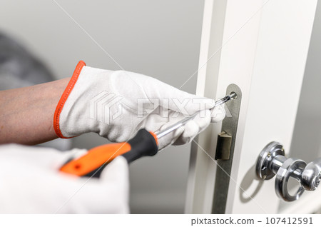 a man in white gloves holds a screwdriver and tightens the lock. a man in white gloves holds a screwdriver and tightens the lock. 107412591