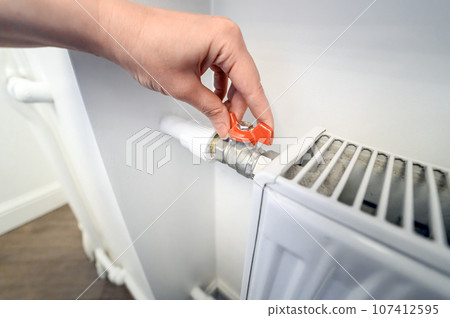 adjusting the heating in the apartment. Woman adjusts temperature on heating radiator, Energy crisis concept. adjusting the heating in the apartment. Woman adjusts temperature on heating radiator, Energy crisis concept. 107412595