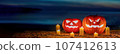 a pair of halloween pumpkin lanterns sitting on a sandy beach at night. 107412613