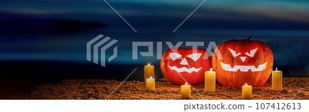 a pair of halloween pumpkin lanterns sitting on a sandy beach at night. 107412613