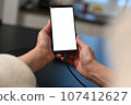 female user holding smartphone in hands, mobile phone white blank screen mockup, using mobile apps at home. 107412627