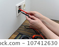 An electrical technician measures voltage using a multimeter tester. Measuring voltage in a socket. 107412630