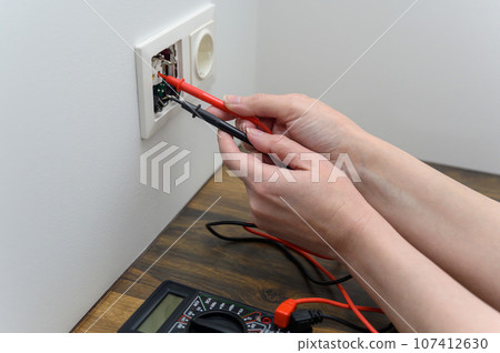 An electrical technician measures voltage using a multimeter tester. Measuring voltage in a socket. An electrical technician measures voltage using a multimeter tester. Measuring voltage in a socket. 107412630