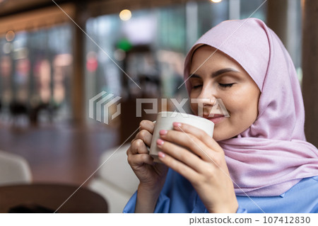 Woman in pink hijab drinking coffee and smiling 107412830