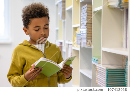 Cute dark-skinned boy in hoodie with a book at school premises Cute dark-skinned boy in hoodie with a book at school premises 107412938