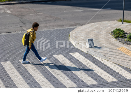 Schoolboy with backpack on his back crossing the street 107412959