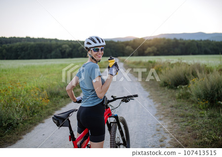 Diabetic cyclist with a continuous glucose monitor on her arm drinking water during her bike tour. 107413515