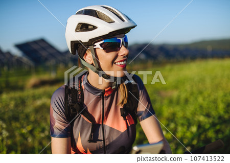 Portrait of a beautiful cyclist standing in front of solar panels at a solar farm. Portrait of a beautiful cyclist standing in front of solar panels at a solar farm. 107413522