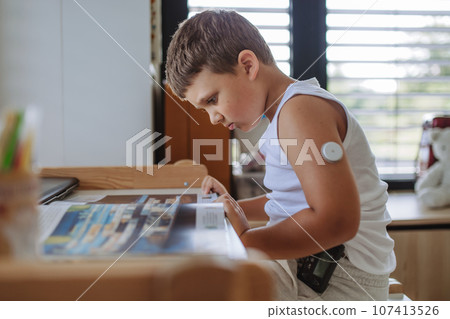 The diabetic boy doing homework, while wearing a continuous glucose monitoring sensor on his arm. 107413526