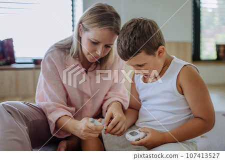 Mother checking her son's blood glucose level at home using a fingerstick glucose meter. Mother checking her son's blood glucose level at home using a fingerstick glucose meter. 107413527