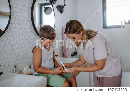 Mother checking her son's blood glucose level at home using a fingerstick glucose meter. Mother checking her son's blood glucose level at home using a fingerstick glucose meter. 107413533