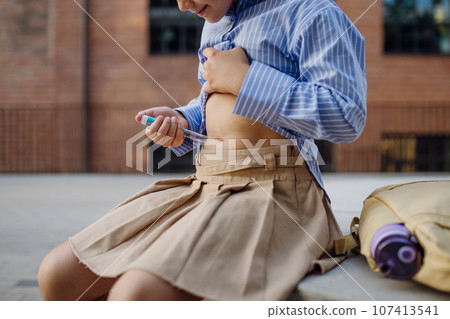 Diabetic schoolgirl injecting insulin in her belly outdoors. Diabetic schoolgirl injecting insulin in her belly outdoors. 107413541