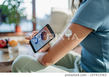 Woman with diabetes checking blood glucose level at home using continuous glucose monitor. Woman with diabetes checking blood glucose level at home using continuous glucose monitor. 107413563