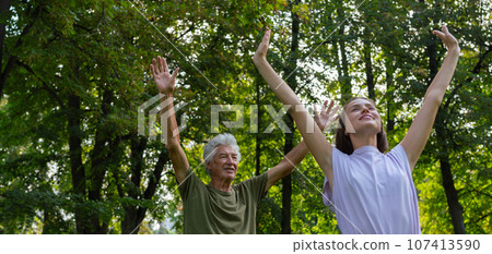 A portrait of a young physiotherapist training outdoors in the park with senior patient. 107413590