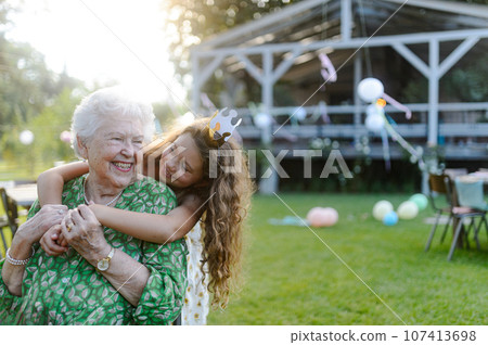 Young girl hugging her elderly grandmother at a garden party. 107413698