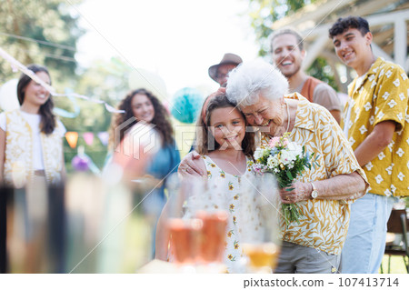 Beautiful senior birthday woman receiving flowers from granddaughter. 107413714