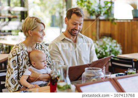 Family with baby reading menu in a restaurant, choosing food and drinks. 107413768
