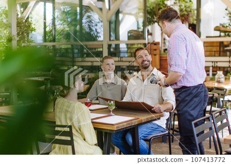Father and children ordering food from a waiter. 107413772