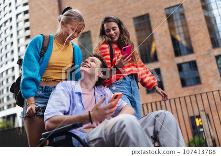 Handsome gen Z boy in a wheelchair with friends in the city. 107413788
