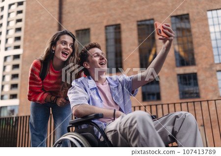 Handsome gen Z boy in a wheelchair with friends in the city. 107413789