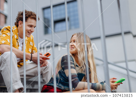 Young Gen Z students meeting outside in the city, sitting on the stairs. 107413815